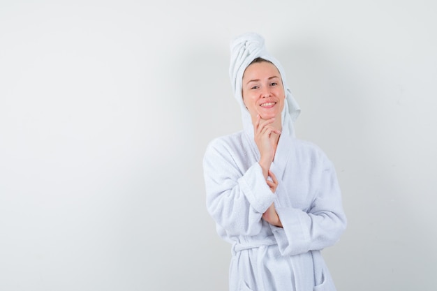 Jeune femme étayant le menton sur place en peignoir blanc, serviette et à la joyeuse, vue de face.