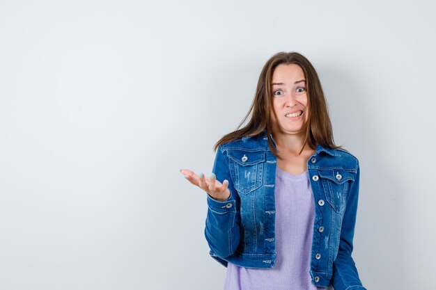 Jeune femme étirant la main dans un geste perplexe en t-shirt, veste et semblant agitée. vue de face.