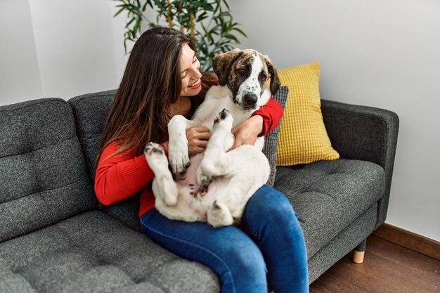 Jeune femme étreignant un chien assis sur un canapé à la maison