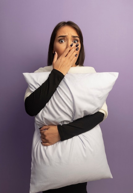 Photo gratuite jeune femme étreignant un oreiller choqué couvrant la bouche avec la main