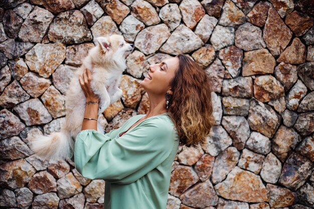 Jeune femme européenne en robe d'été romantique bracelet détient mignon chiot poméranien moelleux spitz à l'extérieur de villa