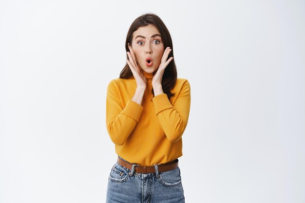 Une jeune femme excitée entend de grandes nouvelles, dit wow et regarde émerveillée sur le blanc