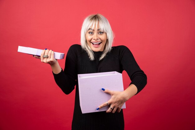 Jeune femme excitée par un cadeau sur un mur rouge.