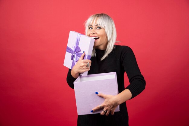 Jeune femme excitée par un cadeau sur un mur rouge.