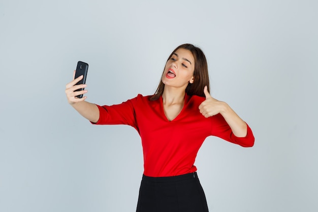 Jeune femme faisant un appel vidéo tout en montrant le pouce vers le haut en chemisier rouge