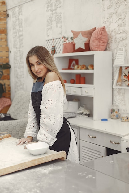 Jeune femme faisant des biscuits en forme pour Noël. Salon décoré de décorations de Noël en arrière-plan. Femme dans un tablier.