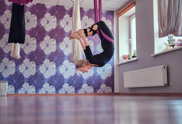 Jeune femme faisant du yoga aérien dans un hamac violet dans un club de fitness.