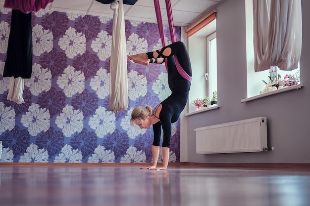 Jeune femme faisant du yoga aérien dans un hamac violet dans un club de fitness.