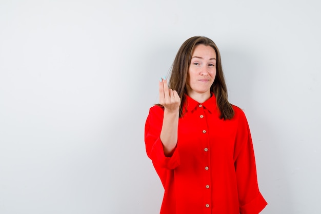 Photo gratuite jeune femme faisant un geste d'argent en chemisier rouge et ayant l'air mécontent. vue de face.