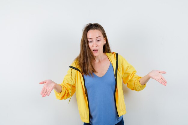 Jeune femme faisant un geste de bienvenue en t-shirt, veste et semblant concentrée, vue de face.