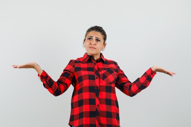 Jeune femme faisant le geste des échelles en chemise à carreaux et à la confusion.