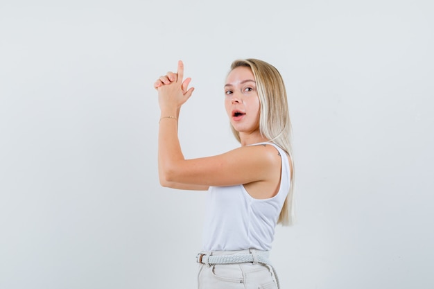 Photo gratuite jeune femme faisant un geste de pistolet en chemisier blanc et à la recherche de prêt