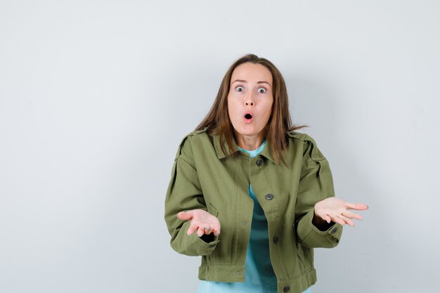 Jeune femme faisant un geste de question en t-shirt, veste et à la perplexité, vue de face.