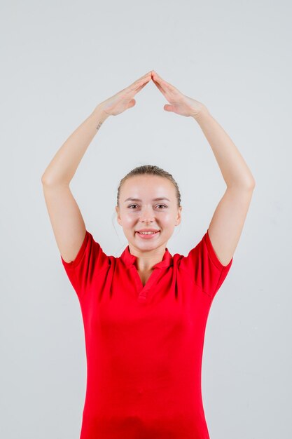 Jeune femme faisant un geste de toit de maison sur la tête en t-shirt rouge et à la joyeuse