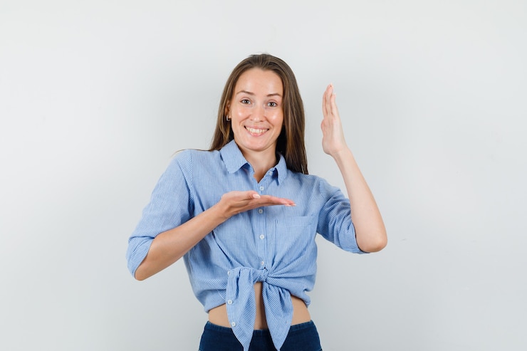 Photo gratuit jeune femme faisant des gestes avec les mains levées en chemise bleue, pantalon et à la joyeuse.