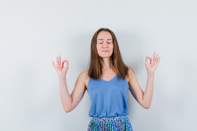 Jeune femme faisant la méditation avec les yeux fermés en maillot, jupe et à la paix