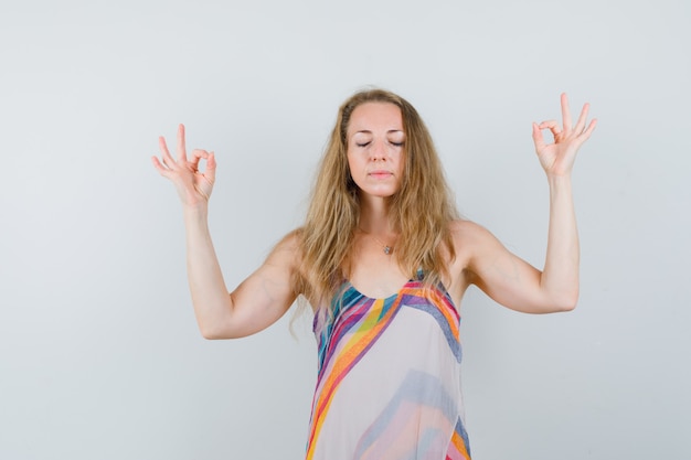 Jeune femme faisant la méditation avec les yeux fermés en robe d'été et à la détente