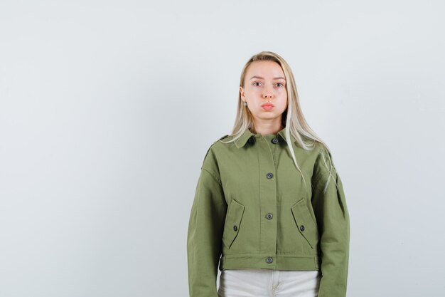 Jeune femme faisant la moue ses lèvres en veste verte et regardant calme, vue de face.