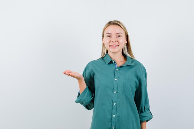 Jeune femme faisant semblant de montrer quelque chose en chemise verte et semblant joyeuse.