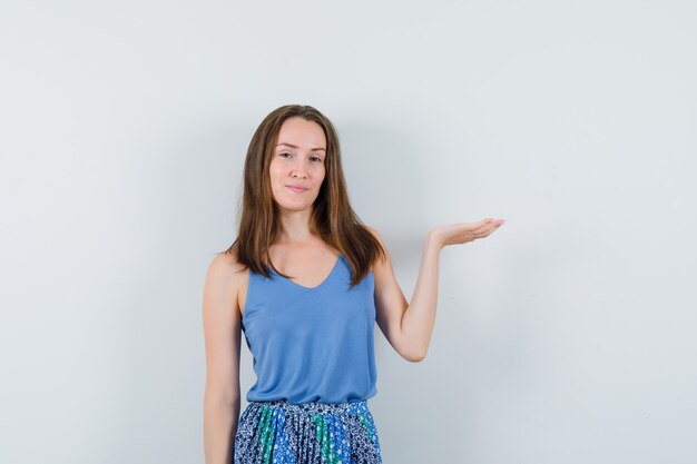 Jeune femme faisant semblant de tenir ou de montrer quelque chose en maillot, jupe et à la vue de face, confiant.