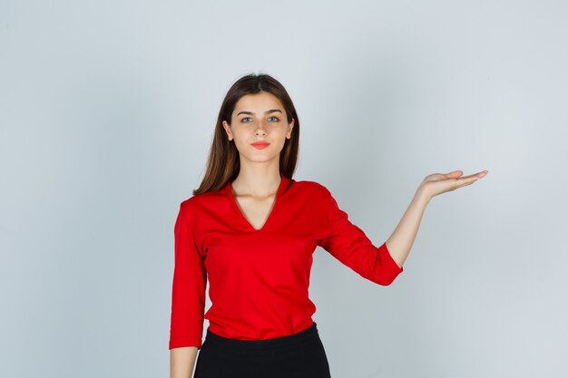 Jeune femme faisant semblant de tenir quelque chose en chemisier rouge, jupe et à la confiance