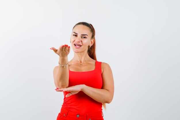 Jeune Femme Faisant Semblant De Tenir Quelque Chose En Débardeur Rouge, Pantalon Et à La Confiance. Vue De Face.