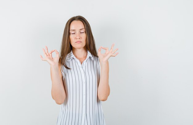 Jeune femme faisant signe ok avec les yeux fermés en t-shirt et à la recherche de calme. vue de face.