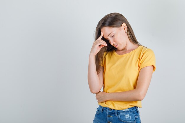 Jeune femme fermant les yeux avec le doigt sur le front en t-shirt, short et à la fatigue