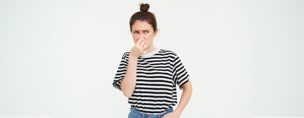 Photo gratuite une jeune femme ferme son nez avec ses doigts à cause de l'odeur dégoûtante isolée sur un fond blanc