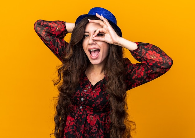 Photo gratuite jeune femme de fête impressionnée portant un chapeau de fête regardant devant faisant un geste de regard en gardant la main sur la tête isolée sur un mur orange