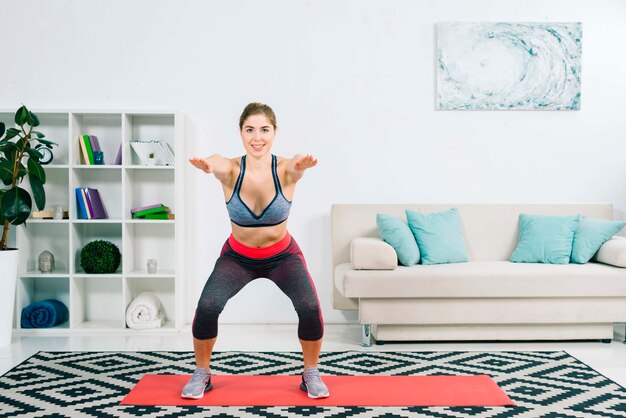 Jeune femme fitness flexible qui s&#39;étend sur le tapis dans le salon moderne