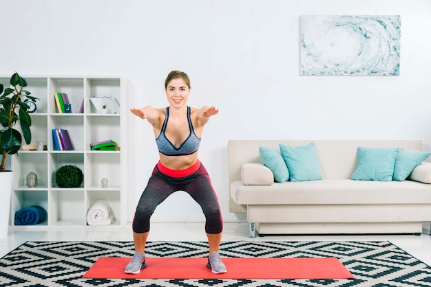 Jeune femme fitness flexible qui s&#39;étend sur le tapis dans le salon moderne