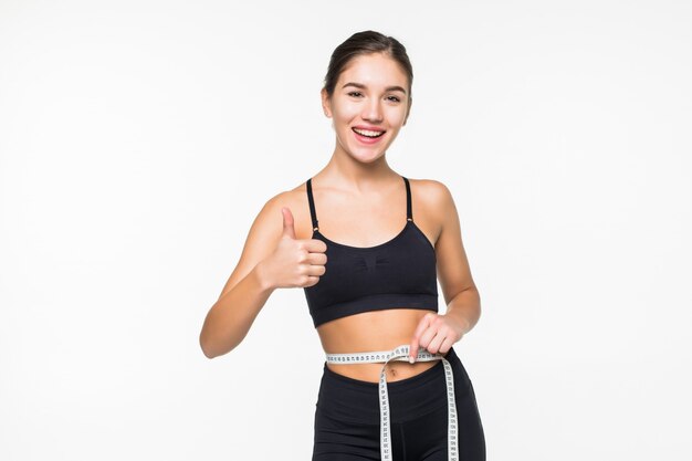 Jeune femme fitness mesure avec du ruban adhésif son ventre isolé sur mur blanc