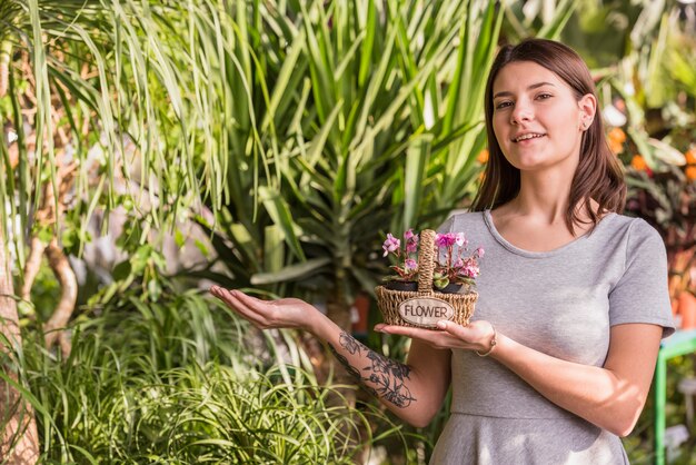 Jeune femme avec des fleurs dans un panier près de plantes vertes