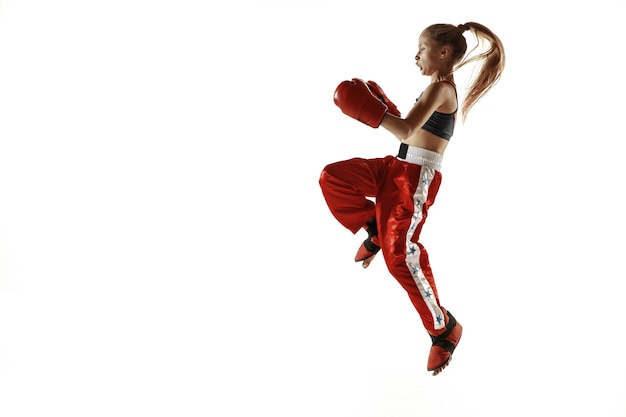 Jeune femme en formation de combattant de kickboxing isolée sur un mur blanc. Fille blonde caucasienne en vêtements de sport rouges pratiquant les arts martiaux. Concept de sport, mode de vie sain, mouvement, action, jeunesse.