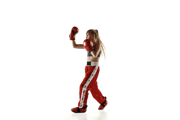 Jeune femme en formation de combattant de kickboxing isolée sur un mur blanc. Fille blonde caucasienne en vêtements de sport rouges pratiquant les arts martiaux. Concept de sport, mode de vie sain, mouvement, action, jeunesse.