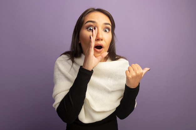 Jeune femme avec un foulard blanc disant un secret avec la main près de la bouche à la surprise