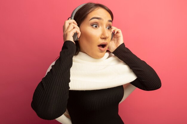 Jeune femme avec un foulard blanc et des écouteurs à côté surpris et étonné