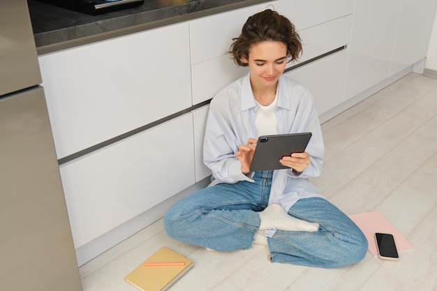 Une jeune femme freelance travaille à domicile, regarde sa tablette numérique, lit des documents en ligne.