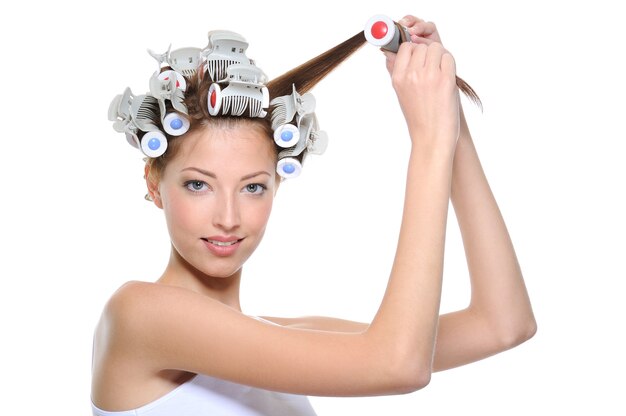 Jeune femme frisant ses cheveux aux bigoudis - isolé sur blanc