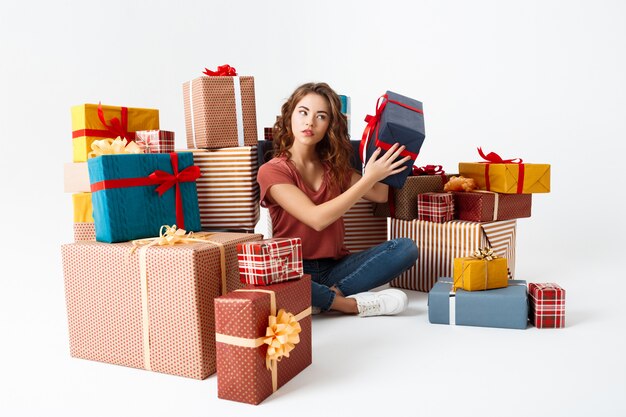 Jeune femme frisée assise sur le sol entre les coffrets cadeaux deviner ce qui est à l'intérieur
