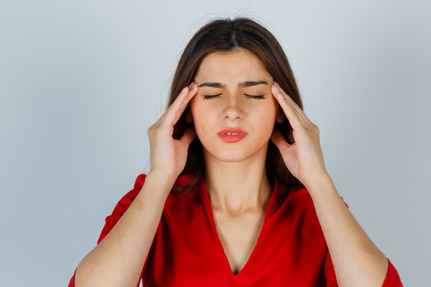 Jeune femme frottant les tempes en chemisier rouge et à la fatigue