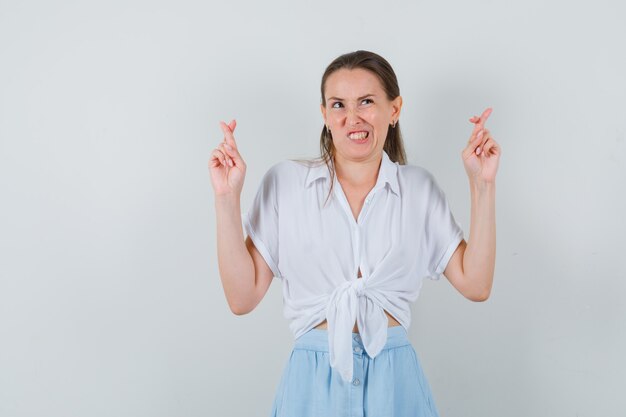 Jeune femme en gardant les doigts croisés en chemisier, jupe et à hésitant