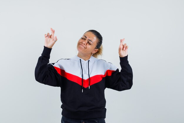 Jeune femme gardant les doigts croisés en sweat-shirt coloré et à la confiance. vue de face.