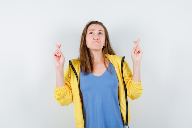 Jeune femme gardant les doigts croisés en t-shirt et l'air triste. vue de face.