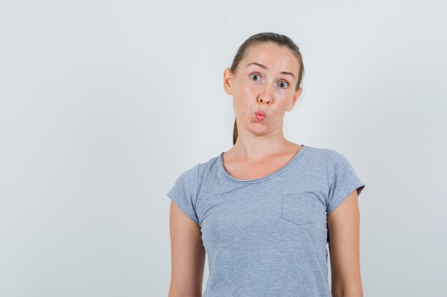 Jeune femme gardant les lèvres pliées en t-shirt gris et à la confusion, vue de face.