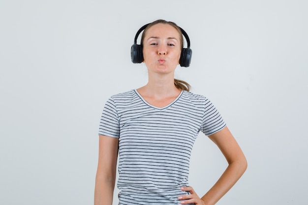 Jeune femme gardant les lèvres pliées en t-shirt rayé, casque, vue de face.