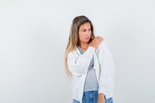 Jeune femme gardant la main sur l'épaule en t-shirt, veste et regardant pensif, vue de face.