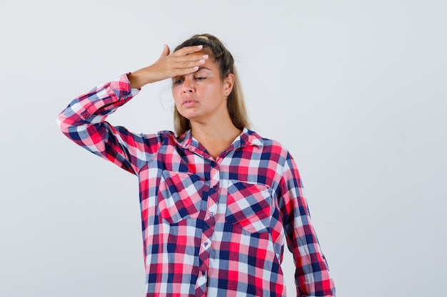 Jeune femme gardant la main sur le front en chemise décontractée et à la fatigue, vue de face.