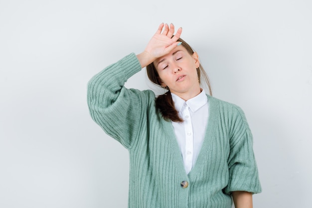 Jeune femme gardant la main sur le front, fermant les yeux en blouse, cardigan et l'air fatigué, vue de face.